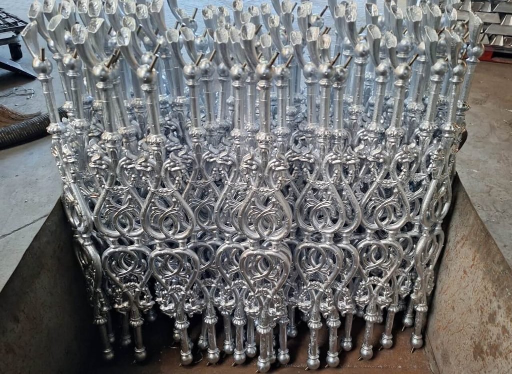 Piezas ornamentales de aluminio fundido apiladas en un contenedor metálico.