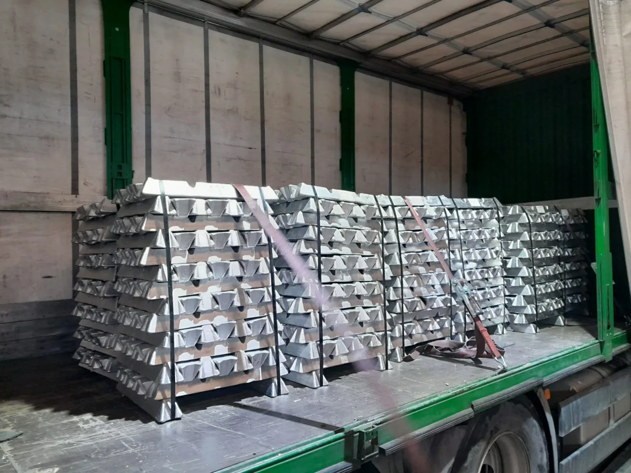 Palés de lingotes de aluminio atados con flejes y cargados en un camión de lona lateral.